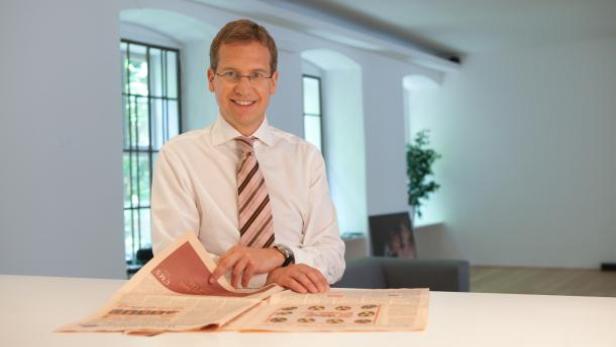 Ein Mann mit Brille und Krawatte liest eine Zeitung an einem Tisch.