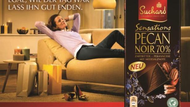 Eine Frau entspannt auf einem Sofa neben einer Tafel Suchard Pecan Noir Schokolade.