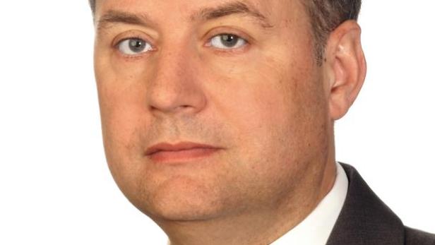 Ein Mann mit Anzug und Krawatte vor einem weißen Hintergrund.