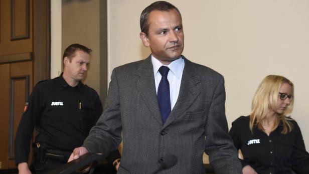 Ein Mann im Anzug wird von zwei Justizbeamten begleitet.