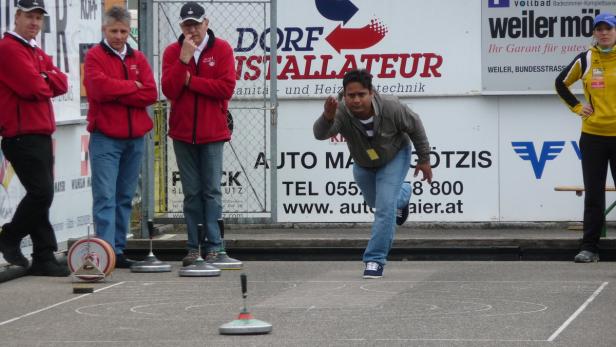Ein Mann spielt Eisstockschießen vor einer Werbewand.