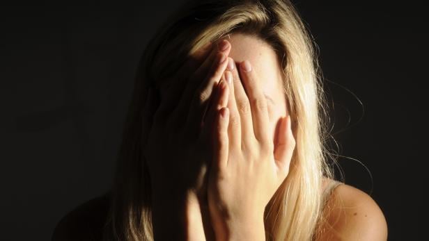 Eine Frau mit blonden Haaren verdeckt ihr Gesicht mit den Händen.