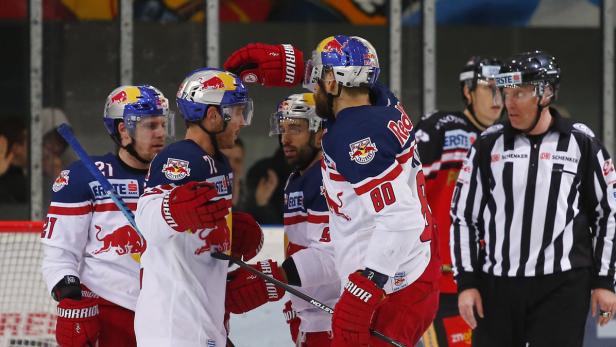 Eishockeyspieler von Red Bull begrüßen sich auf dem Eis, während ein Schiedsrichter zusieht.