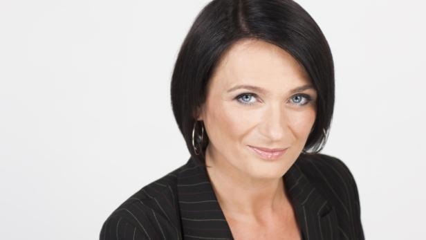 Eine Frau mit dunklen Haaren und einem gestreiften Blazer lächelt in die Kamera.