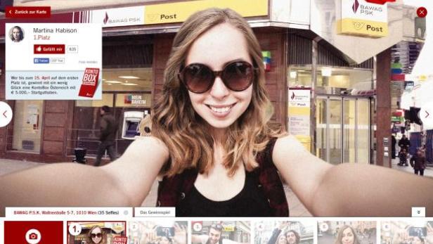 Eine junge Frau macht ein Selfie vor einer BAWAG P.S.K. Filiale in Wien.