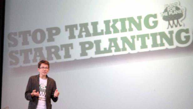 Ein junger Mann hält einen Vortrag vor dem Hintergrund „Stop Talking, Start Planting“.