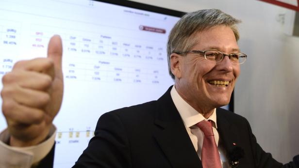 Ein lächelnder Mann im Anzug gibt vor einer Wahltabelle den Daumen hoch.
