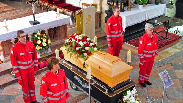 Mitglieder des Roten Kreuzes stehen Wache an einem mit Blumen geschmückten Sarg in einer Kirche.