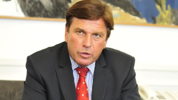 Ein Mann in Anzug und Krawatte sitzt an einem Tisch.