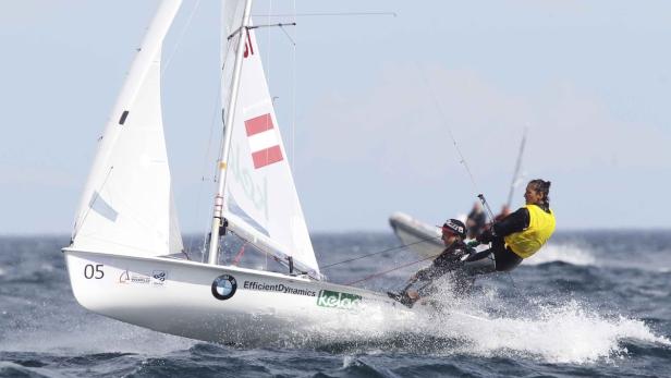 Zwei Segler steuern ein Segelboot mit österreichischer Flagge auf dem Meer.