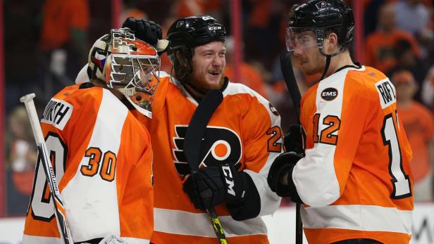 Drei Eishockeyspieler der Philadelphia Flyers in ihren Trikots stehen zusammen.