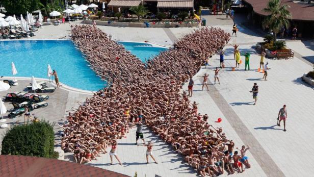 Eine große Gruppe von Menschen formt ein X neben einem Schwimmbad.