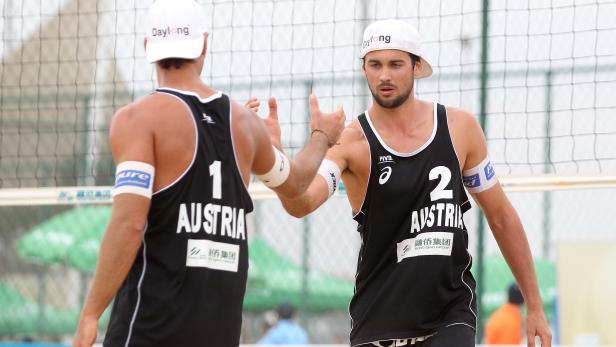 Zwei Beachvolleyballspieler aus Österreich geben sich ein High-Five am Netz.