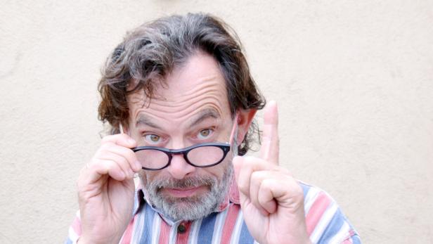 Ein Mann mit Brille hält mahnend den Zeigefinger hoch.