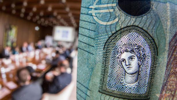 Nahaufnahme eines Euroscheins mit dem Porträt der Europa, im Hintergrund ein Konferenzraum.