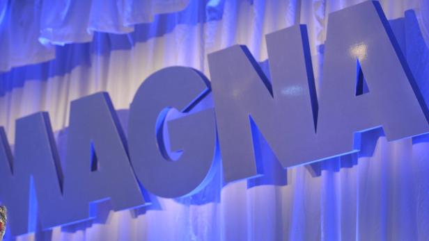 Der Schriftzug „MAGNA“ vor einem weißen Vorhang mit blauer Beleuchtung.