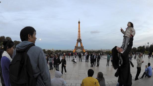 Eine Frau hält ein Kind auf ihren Schultern vor dem Eiffelturm in Paris.