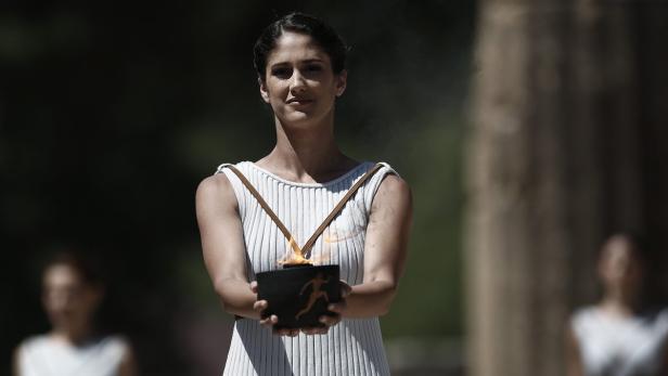Eine Frau im weißen Kleid hält die olympische Fackel.