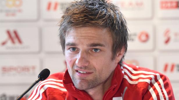 Ein Mann in einer roten Jacke spricht in ein Mikrofon.