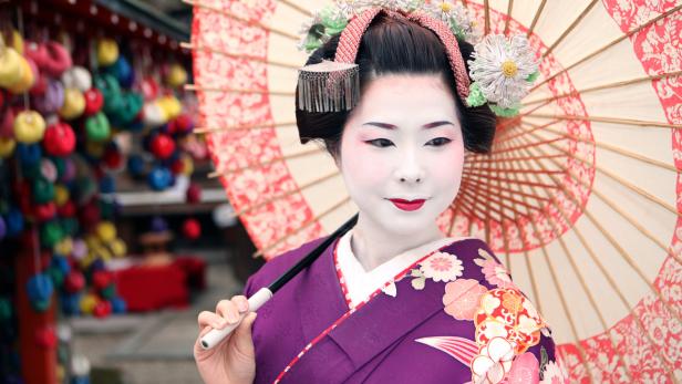 Eine Geisha mit traditionellem Make-up und einem verzierten Sonnenschirm.