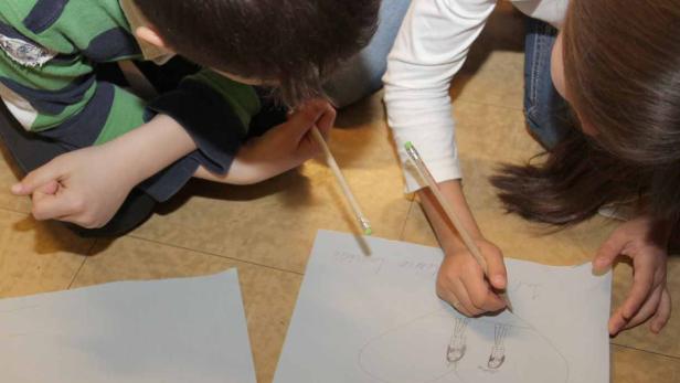 Zwei Kinder zeichnen gemeinsam ein Bild mit der Aufschrift „Familie“.