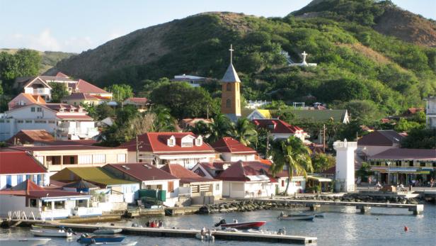 Eine Küstenstadt mit roten Dächern, einer Kirche und einem Denkmal auf einem Hügel.