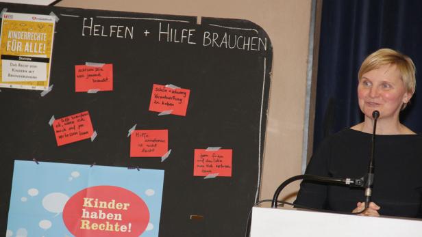 Eine Frau spricht an einem Rednerpult vor einer Tafel zum Thema Kinderrechte.