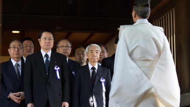 Eine Gruppe japanischer Männer in Anzügen steht vor einem Shinto-Priester.
