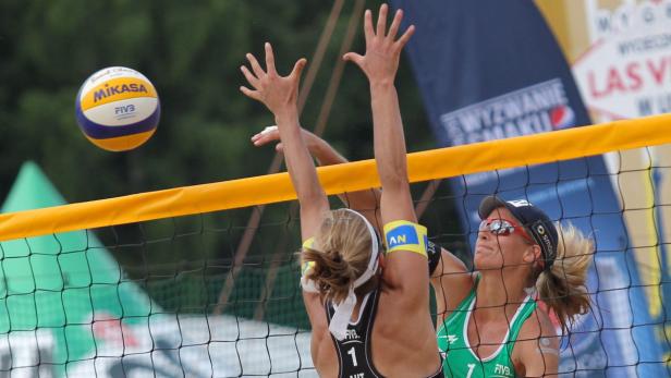 Zwei Beachvolleyballspielerinnen springen am Netz, um einen Ball zu blocken.