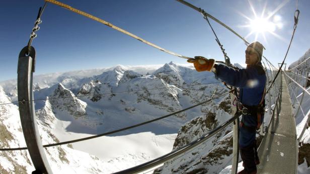 Eine Person steht auf einer Hängebrücke in den schneebedeckten Bergen.