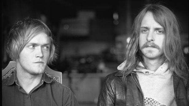 Zwei junge Männer sitzen nebeneinander in einem Schwarzweißfoto.