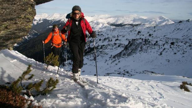 Zwei Skifahrerinnen steigen in einer verschneiten Berglandschaft auf.