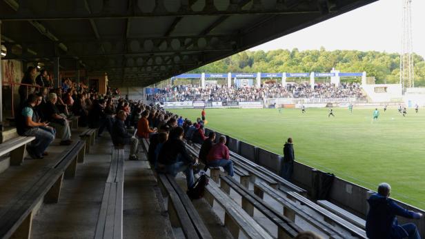 Zuschauer sitzen auf der Tribüne bei einem Fußballspiel.