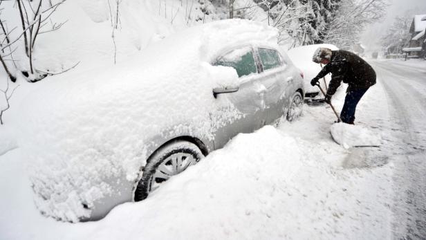 Eine Person schaufelt Schnee von einem Auto frei.