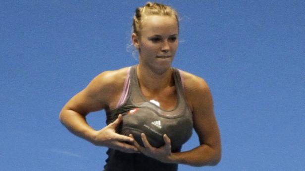 Caroline Wozniacki hält einen Tennisball vor blauem Hintergrund.