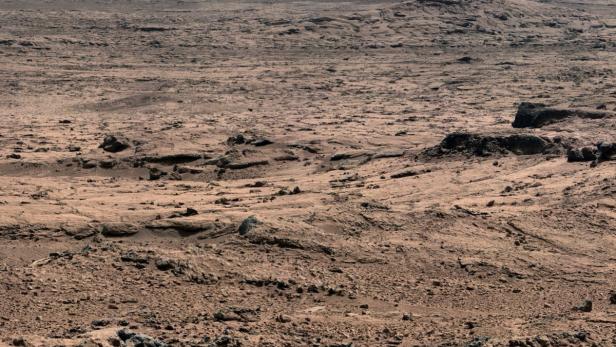 Eine karge, rote Landschaft mit Hügeln im Hintergrund.