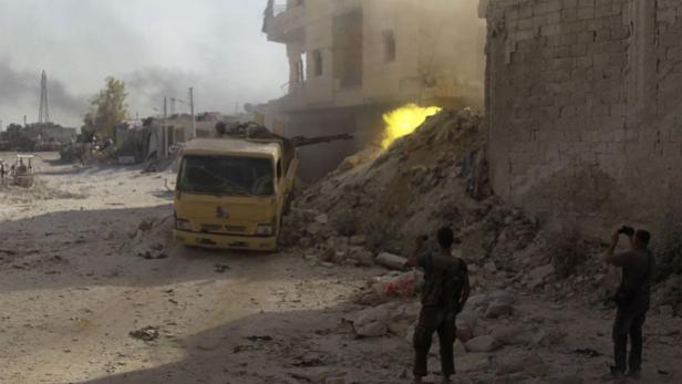 In einer zerstörten Stadt steht ein gelber Lastwagen mit montiertem Geschütz.