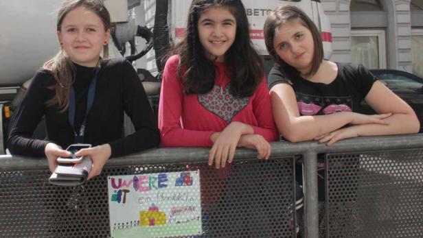 Drei junge Mädchen stehen an einer Absperrung vor einem LKW.