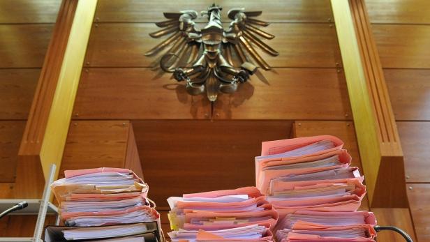 Ein Gerichtssaal mit Aktenstapeln und einem Bundesadler an der Wand.