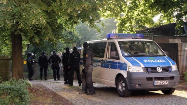 Polizisten stehen neben einem Einsatzwagen vor einem Gebäude.