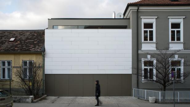 Eine Person geht vor einem modernen Gebäude mit weißer Fassade entlang.