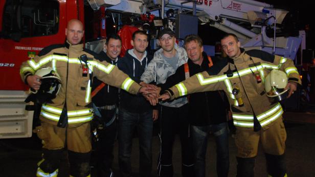 Eine Gruppe Feuerwehrleute posiert vor einem roten Feuerwehrauto und legt ihre Hände übereinander.
