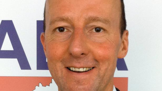 Porträt eines lächelnden Mannes vor einem Logo.