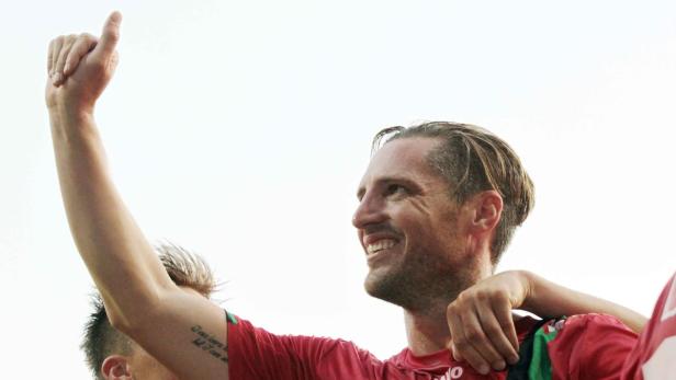 Ein lächelnder Fußballspieler mit erhobenem Daumen feiert einen Sieg.