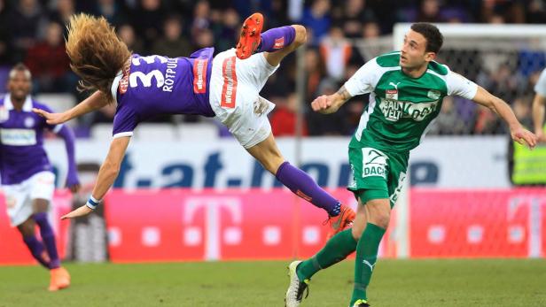 Ein Fußballspieler in lila Trikot führt einen Fallrückzieher aus, während ein Gegenspieler zusieht.