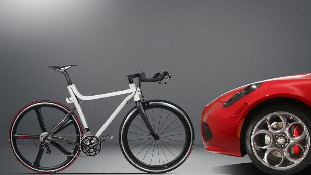 Ein weißes Alfa Romeo Fahrrad steht neben einem roten Alfa Romeo Sportwagen.