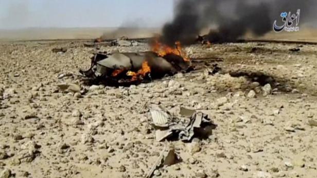 Die Überreste eines brennenden Flugzeugs liegen in einer Wüstenlandschaft.