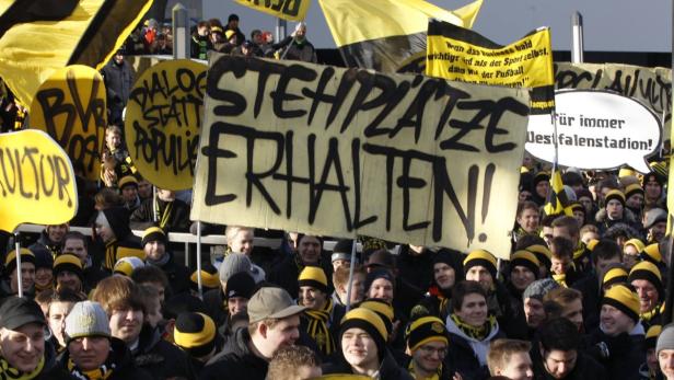 Eine Menschenmenge hält Schilder mit Aufschriften wie „Stehplätze erhalten!“ und „Für immer Westfalenstadion!“.
