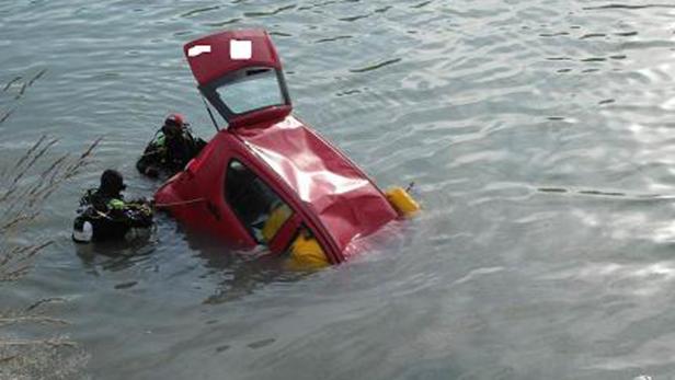 Ein rotes Auto liegt im Wasser, während Taucher in der Nähe sind.