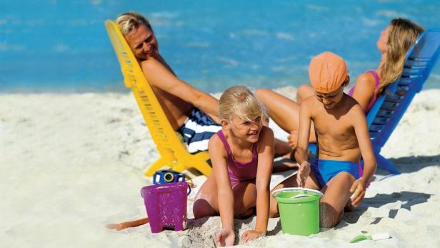 Eine Familie entspannt am Strand, während die Kinder mit Eimern im Sand spielen.